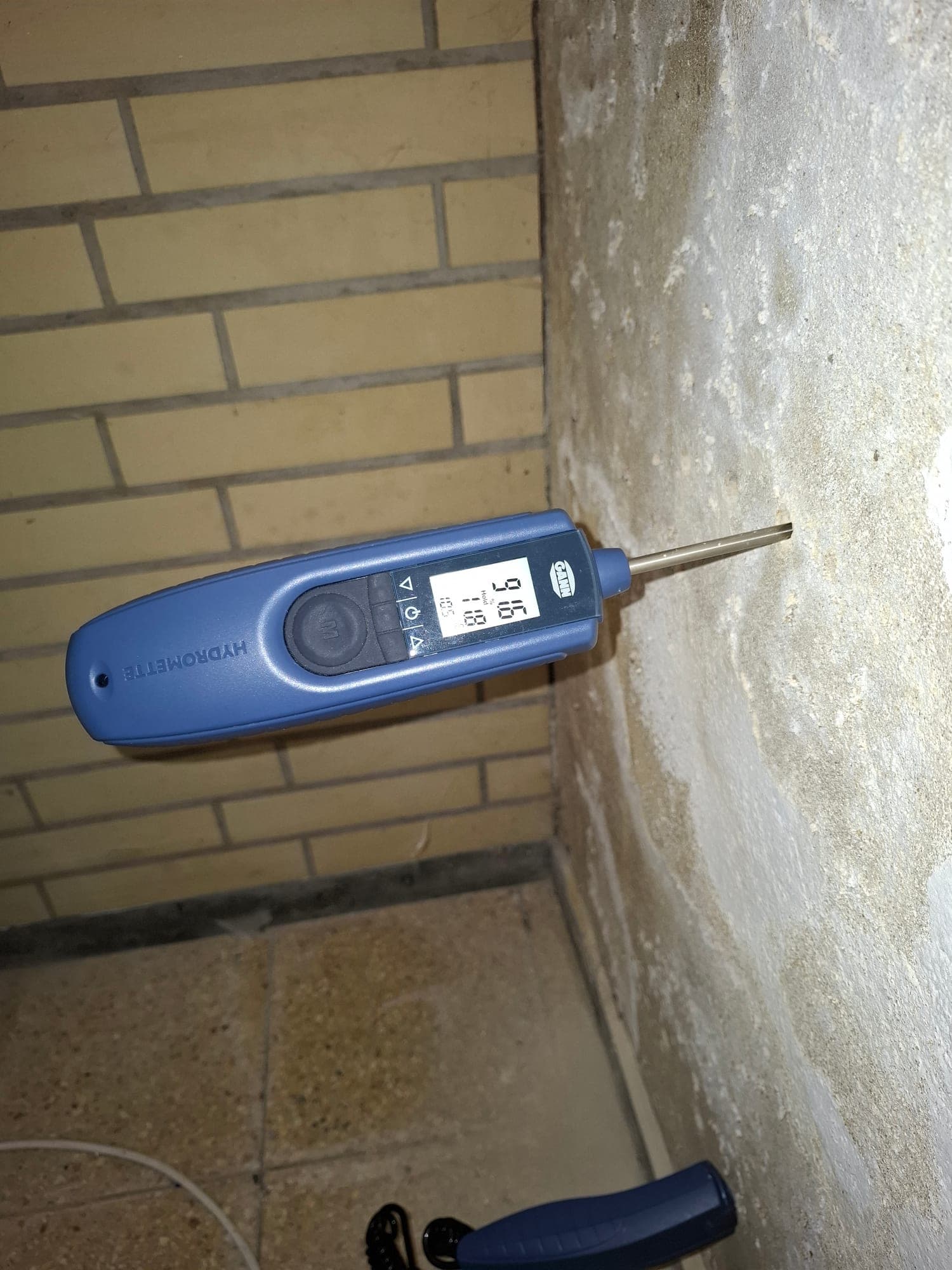 Feuchtemessgerät an einer durchfeuchteten Kellerwand, die Anzeige zeigt 96 % Materialfeuchte